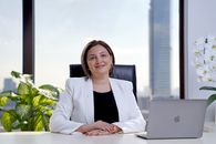 Professional woman smiling at desk with skyscraper view, representing corporate leadership.